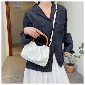 Detailed view of white pleated cloud bag with round wooden handle worn as crossbody