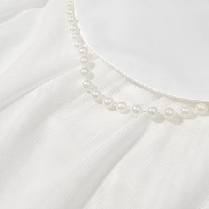 Detailed view of elegant pearl ornaments on the neckline of a white satin evening dress