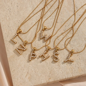 Detail of 18K gold plated snake chains and white pearl letter pendants on marble
