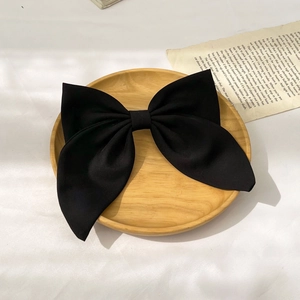 Detailed view of large black fabric bow hair clip on a vintage book page and wooden tray