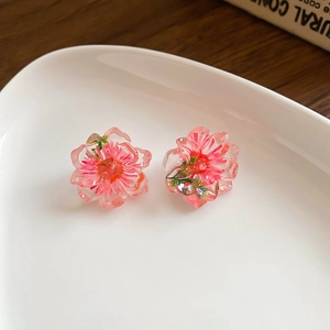 Detailed macro view of pink floral stud earrings with resin petals on a white ceramic plate