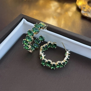 Detailed close-up of golden C-shaped hoop earrings with green oval stones in a box