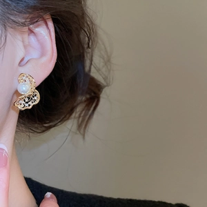 Close-up of golden hollow twisted earrings with pearls worn by a model in warm light