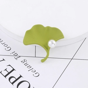 Elegant green ginkgo leaf brooch with white pearl detail on minimalist white stand