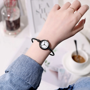 Close-up of minimalist bangle watch with twisted black band and white quartz dial