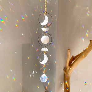 Moon phase suncatcher with crystal ball reflecting rainbow light on a beige wall