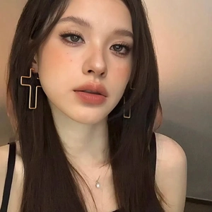Close-up of a model wearing large hollow gold cross earrings with a pearl necklace