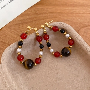 Macro detail of retro hoop earrings featuring tiger eye, pearl, and black stone beads