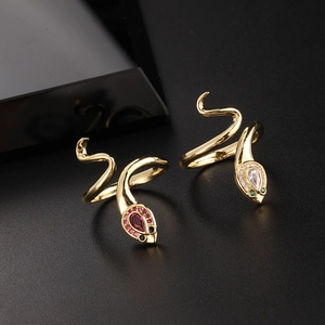 Macro detail of gold snake-shaped open rings with red and green gemstone eyes and pavé stones