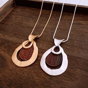 Close-up of vintage textured metal necklaces with woven wood details on a wooden tray