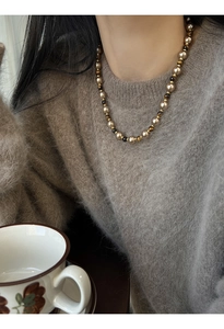 Détail d'un collier de perles plaqué or avec œil de tigre sur un pull gris doux