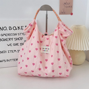 Detail of pink canvas tote bag featuring heart prints and woven orange handle straps