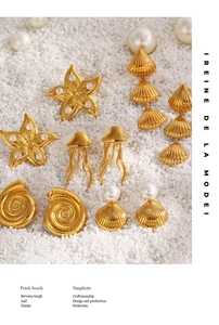 Detailed view of gold ocean-themed earrings with starfish and pearls on a white sandy beach