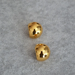 Close-up of polished golden spherical stud earrings on a grey textured surface