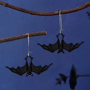 Macro shot of matte black bat earrings hanging on dry branches with gothic blue background