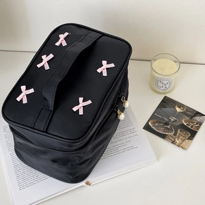 Detail of black cosmetic bag featuring a pink bow and pearl zipper charm detail