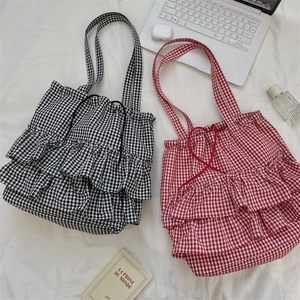 Detail of plaid tote bags with layered ruffles and drawstring closure on a white fabric