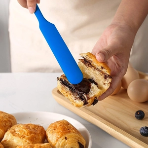 Blue silicone spatula spreading jam on chocolate bread in a cozy kitchen setting