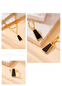 Macro detail of gold layering necklace and earrings with black trapezoid charms
