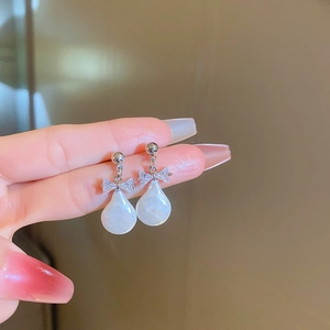 Close-up of bow knot earrings featuring white drop pearls and sparkling zircon stones