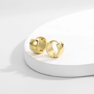 Detailed view of wide gold titanium steel huggie earrings on minimalist stone display