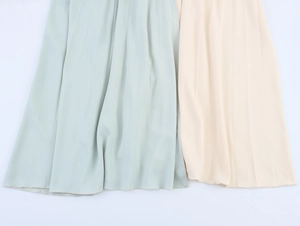 Detail of elegant pleated dress hem in light sage green and creamy beige chiffon fabric