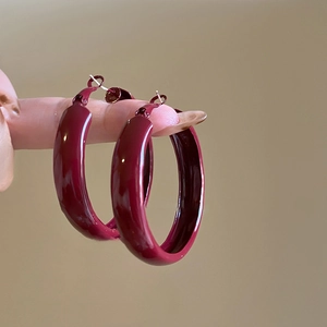 Close-up of deep red glossy hoop earrings showing the smooth lacquer finish and C-shape