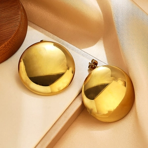 Détail de boucles d'oreilles rondes plaquées or sur soie champagne et plateau bois