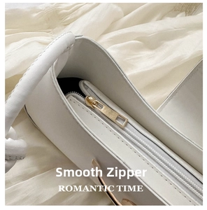 Close-up of smooth silver zipper and light gold hardware on white leather shoulder bag