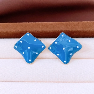 Close-up of blue diamond-shaped stud earrings with white polka dots and gold trim