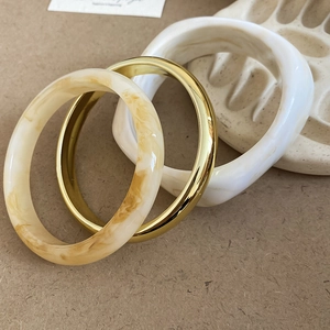 Three-piece set of resin and gold metal bangles with marble texture on a ceramic tray