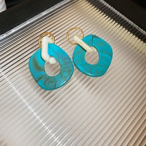 Macro view of blue marble resin earrings with gold metal hoops on textured glass