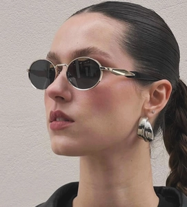 Close-up of oval sunglasses with metallic gold temples and oversized silver hoop earrings