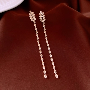 Détail de boucles d'oreilles feuilles dorées 18K avec pompons en zircon sur soie sombre