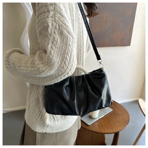 Detail of a black pleated cloud bag featuring a pearl handle and detachable crossbody strap