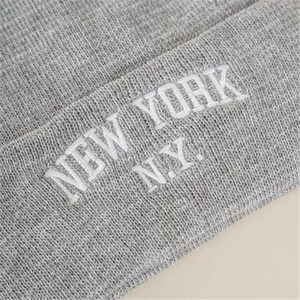 Macro shot of gray knitted beanie showing white New York N.Y. embroidery and thick fabric texture