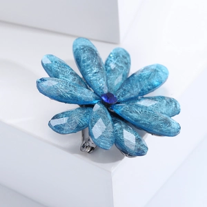 Detailed macro shot of blue acrylic flower brooch with silver textures and gemstone