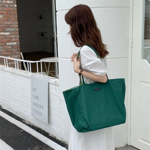 Detail view of large dark green canvas tote bag styled on model in an urban outdoor setting