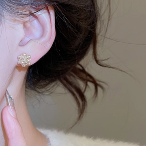 Detail of elegant gold flower earrings with pearls and diamonds worn by a model