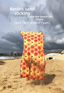 Sand-free double-sided fleece beach towel with orange sunflower print shown on the sand