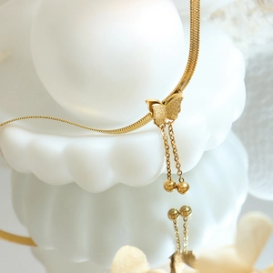 Elegant gold butterfly tassel necklace with steel beads on a wavy white pedestal