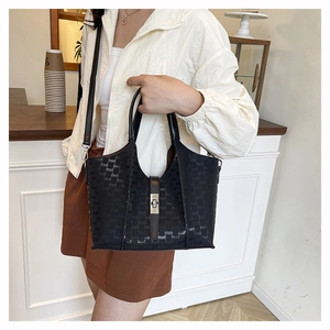 Close-up of black tote bag with monogram pattern and leather strap held by a model