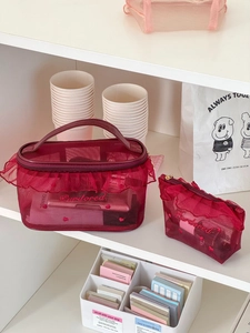 Detail of red mesh makeup bag set with ruffle trim and embroidered lettering on a shelf