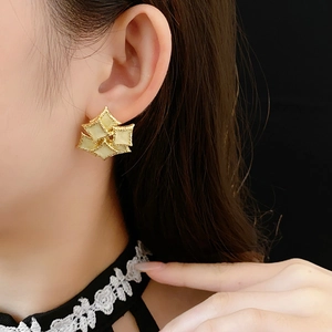 Close-up of vintage gold windmill earrings with beige enamel inlay worn by a model