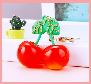 Close-up of artificial resin red cherry keychain with rhinestone green leaf details