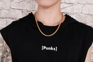 Polished gold box chain necklace shown on male model against white brick wall