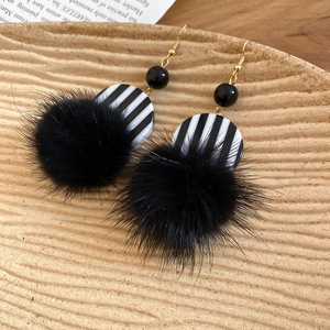 Close-up of vintage resin earrings with black faux fur pompom on a brown textured tray