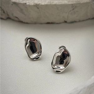 Detailed view of silver liquid metal earrings on a textured stone over light grey backdrop