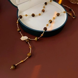 Detailed close-up of tiger eye bead necklace with a leaf pendant on a jewelry box