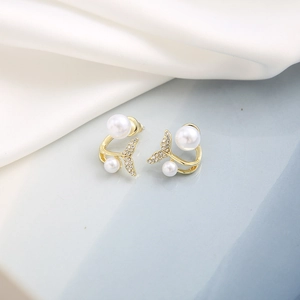 Close-up of golden mermaid tail earrings with pearls and crystals on silk fabric